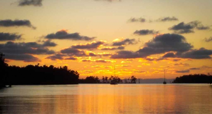 a sailboat floats in the distance in calm water at sunset